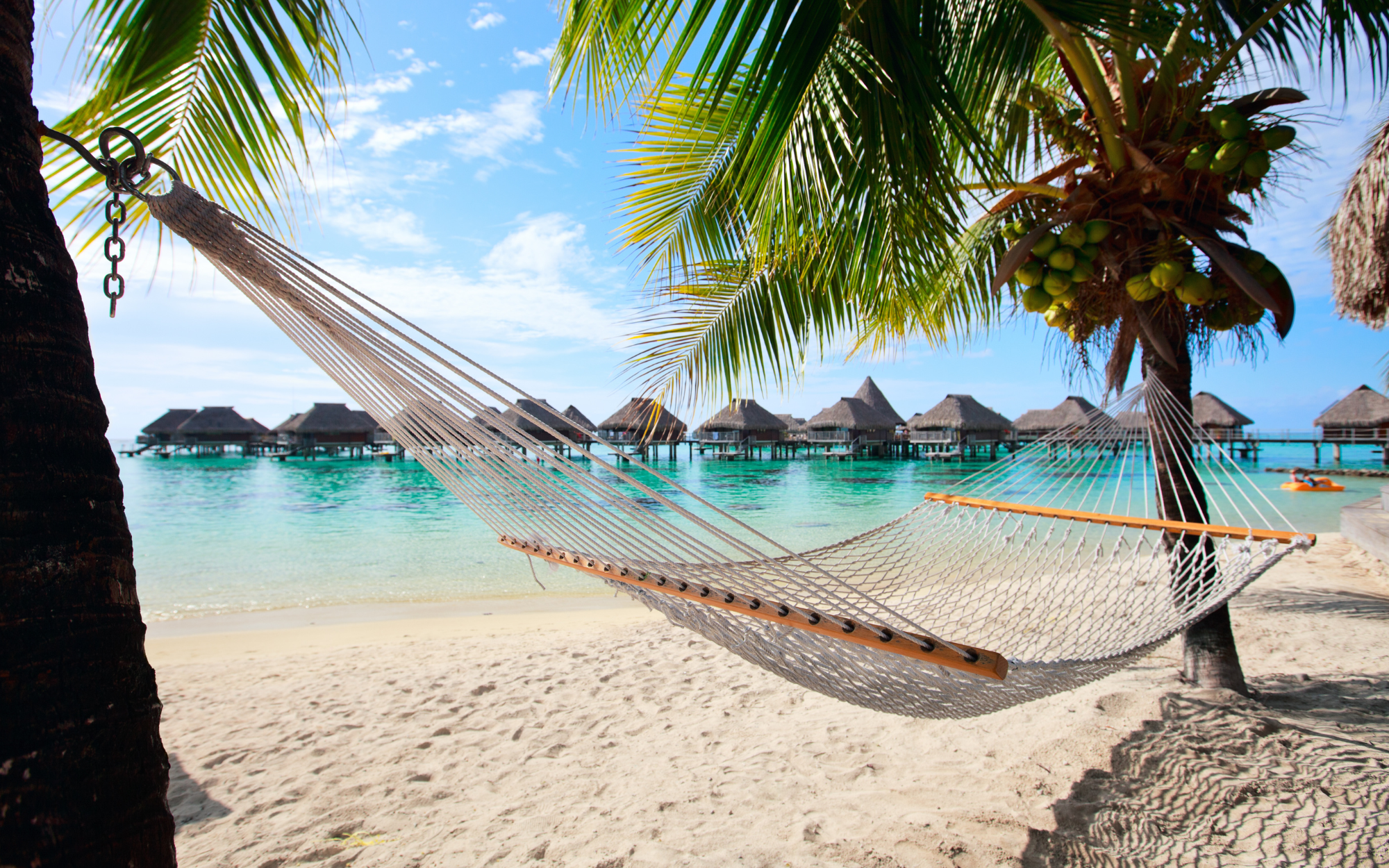Hammock on the beach with overwater bungalows in the background